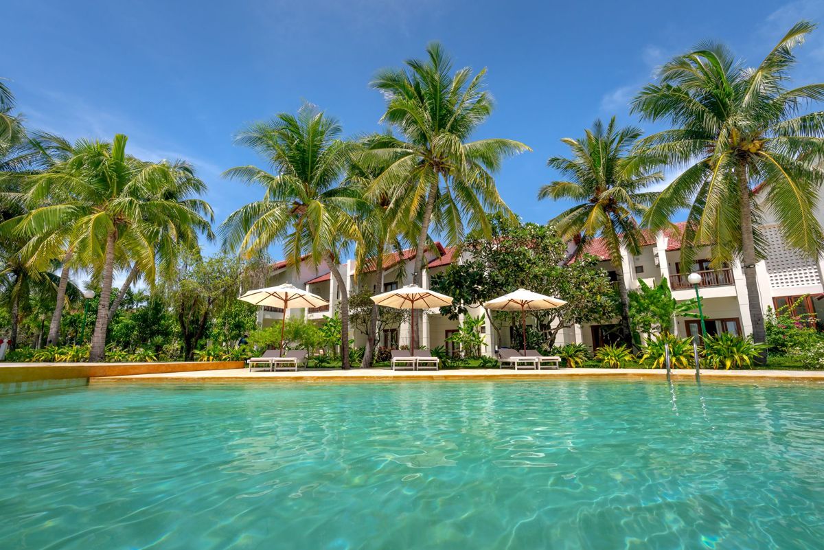 Resort pool lined with palm trees in front of low-rise guest buildings