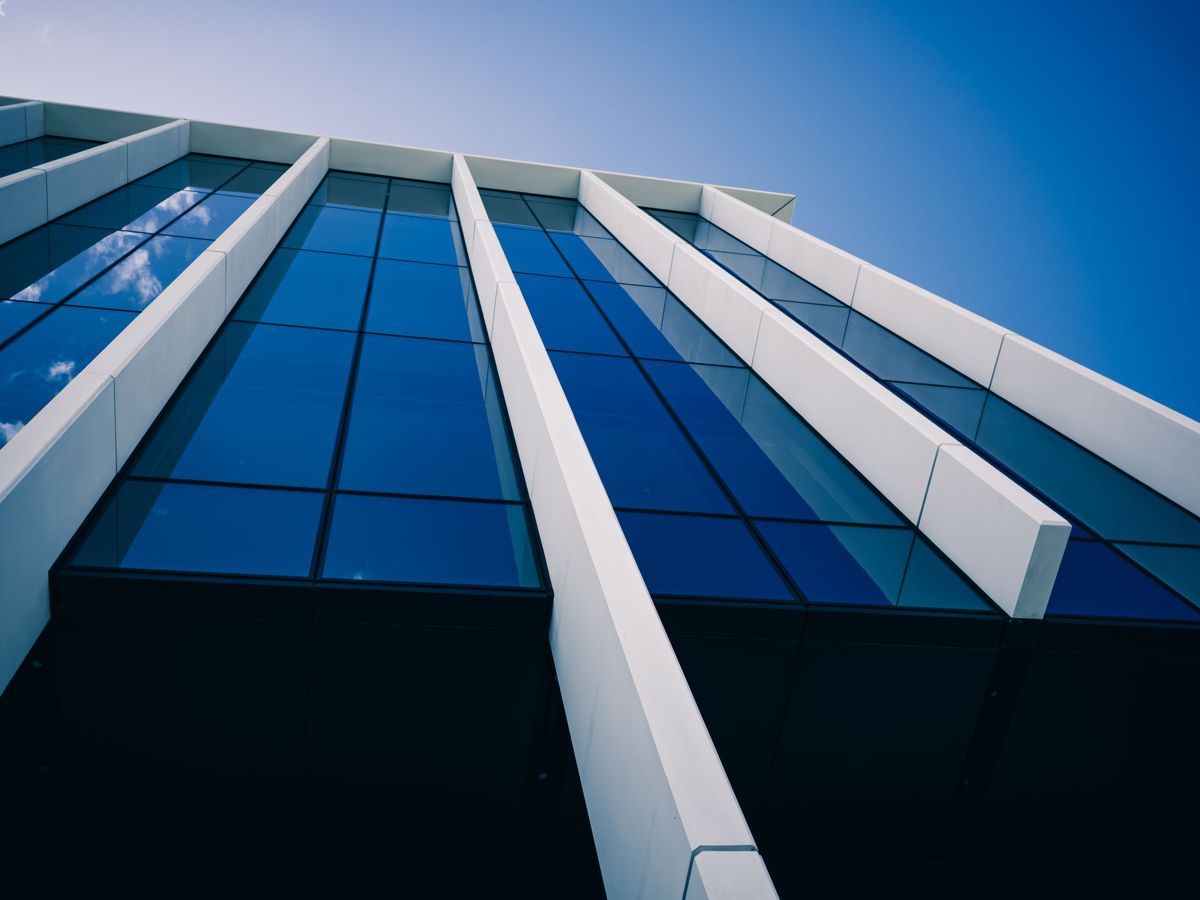Looking up at a glass and white-fin office building facade against a blue sky